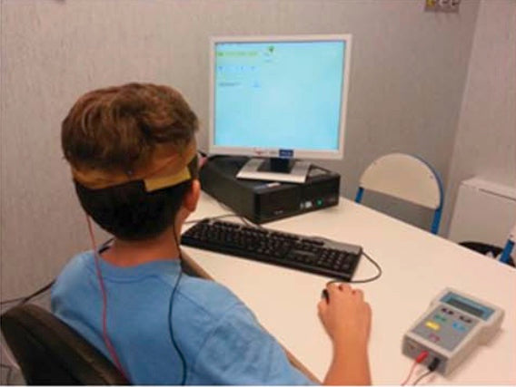 A child wearing stimulation electrodes reads at a computer during a training session