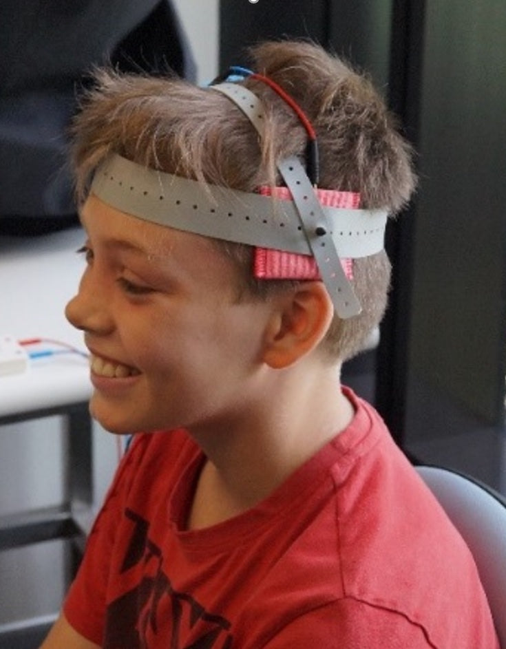 A smiling child wearing a stimulation headband with sponge electrodes during a session