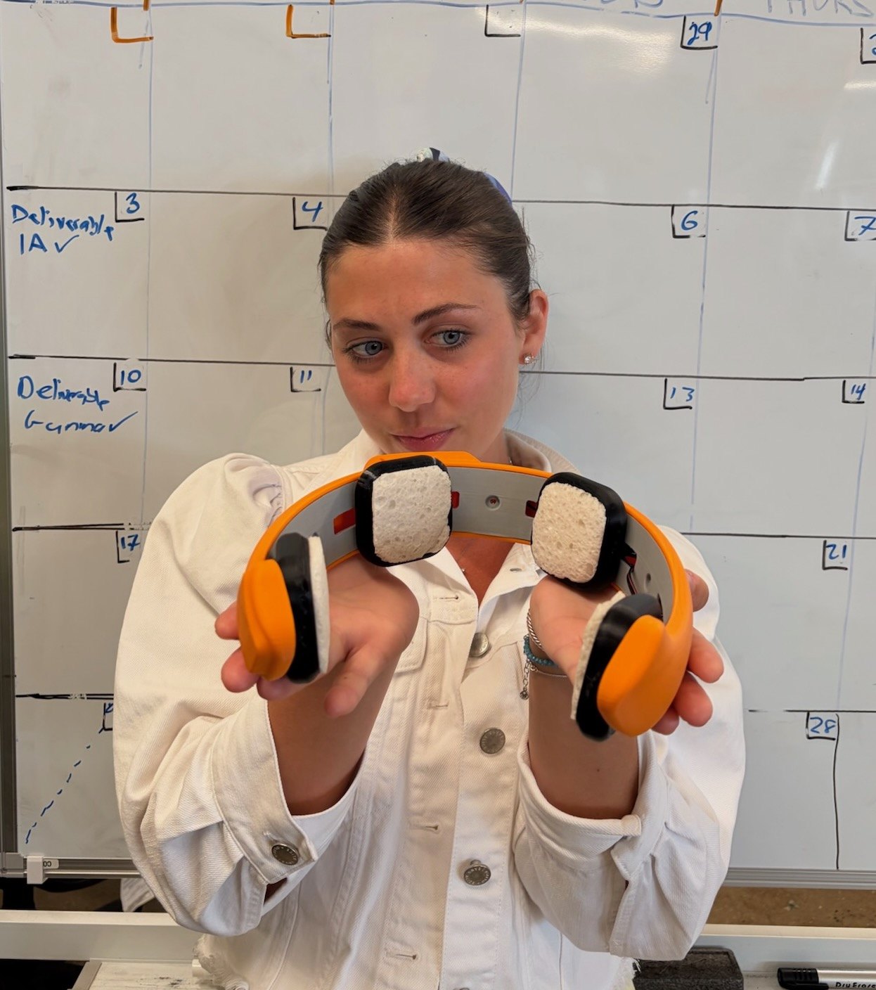Next-generation General Neuroscience tES headset: an orange 3D-printed band with sponge electrodes, held toward the camera