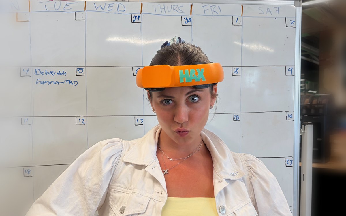Woman wearing an orange HAX headband in front of a whiteboard, pouting at the camera