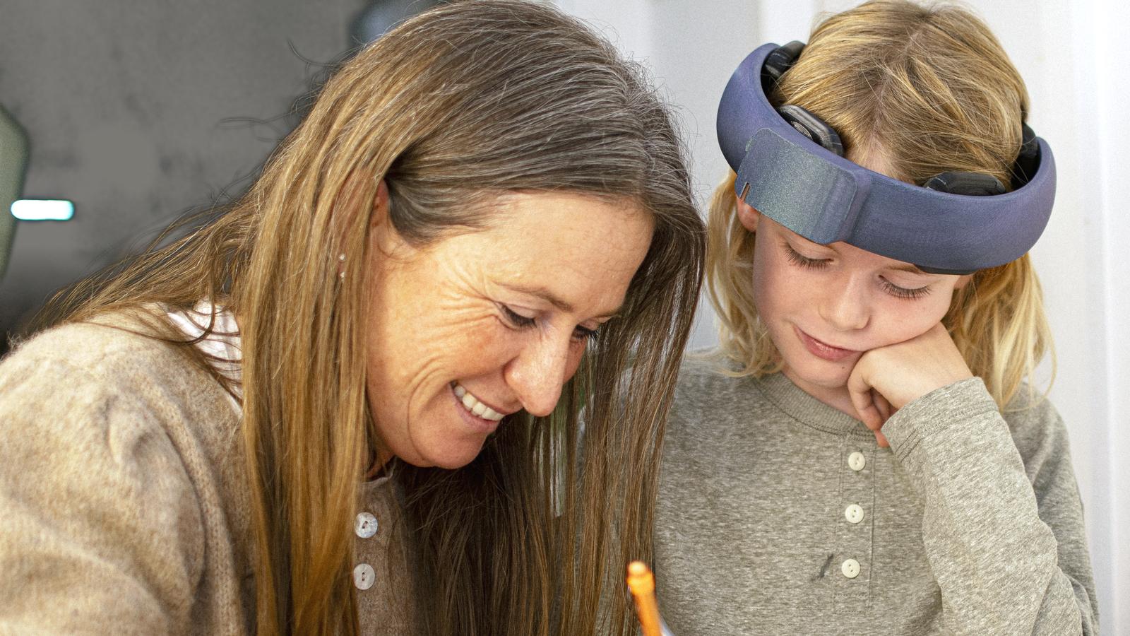 A parent and a child wearing the NeuroLingo headband smile down at a workbook together